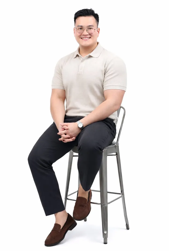 Davis Lim, PropNex property agent, seated on a bar stool in a beige polo shirt